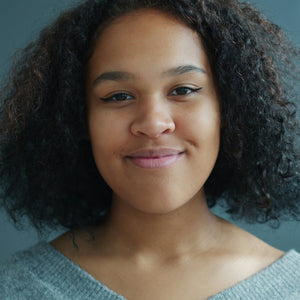 Woman with curly hair wearing a light gray sweater against a neutral background